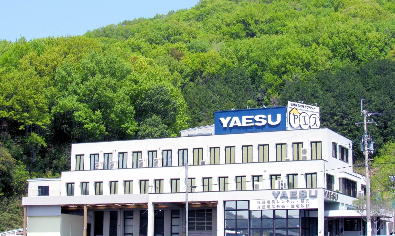 写真：株式会社ヤエスの本社。裏には青々した山が広がっている。
